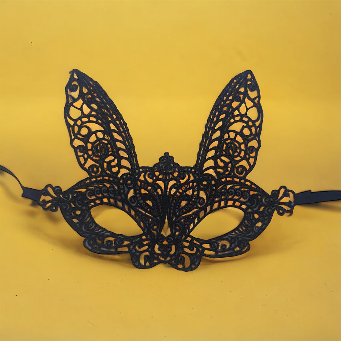 Black lace rabbit-shaped masquerade mask with a tie-back design, against a yellow background.