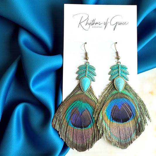 Peacock feather earrings on a blue satin background with 'Rhythms of Grace' branding.