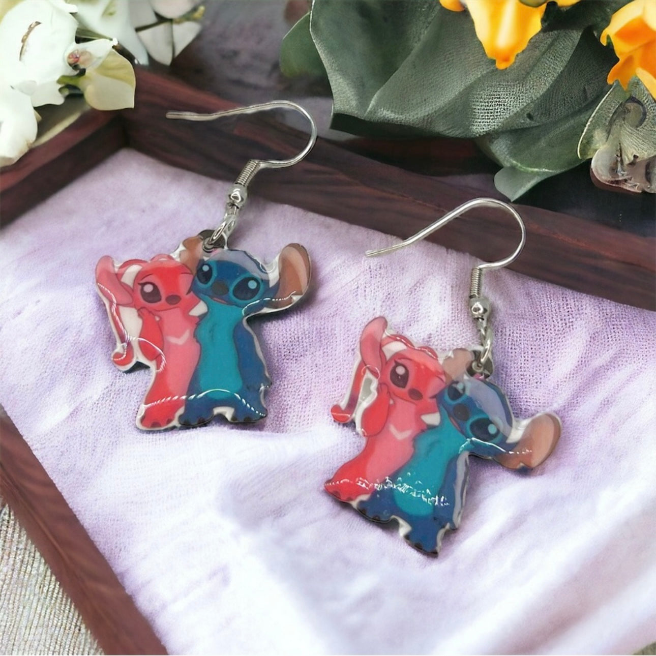 Pair of cartoon character earrings on a white cloth with flowers in the background