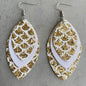 Three pairs of mermaid tail-shaped earrings displayed on cards, with the ocean in the background. Each earring features a unique color pattern with white, gold, purple, and green elements.