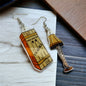 A pair of earrings designed like a leg lamp from the movie 'Christmas Story', with the lamp shade in orange and the base in brown color, displayed on a wooden surface.
