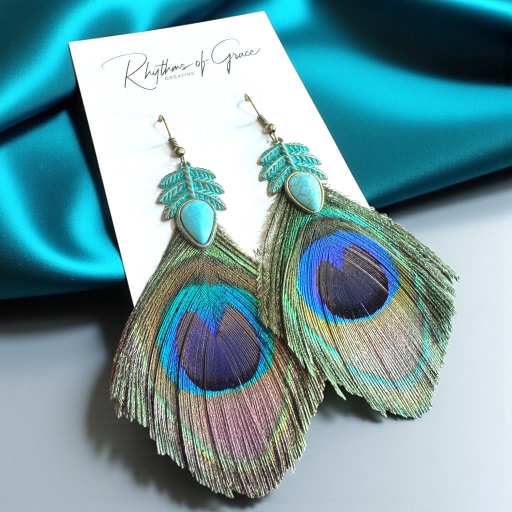 Peacock feather earrings on a display card with a blue satin background