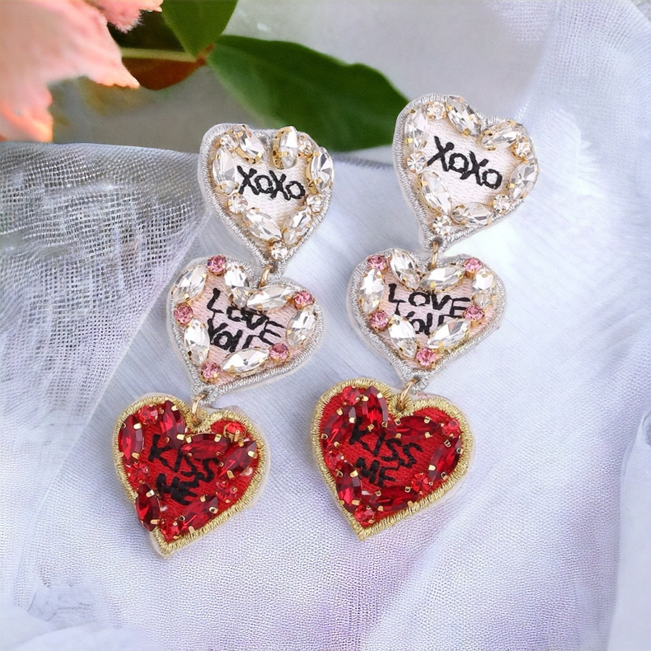 A pair of beaded heart-shaped earrings with red and clear beads, featuring the words 'XOXO' and 'I LOVE YOU' written in a cursive script.