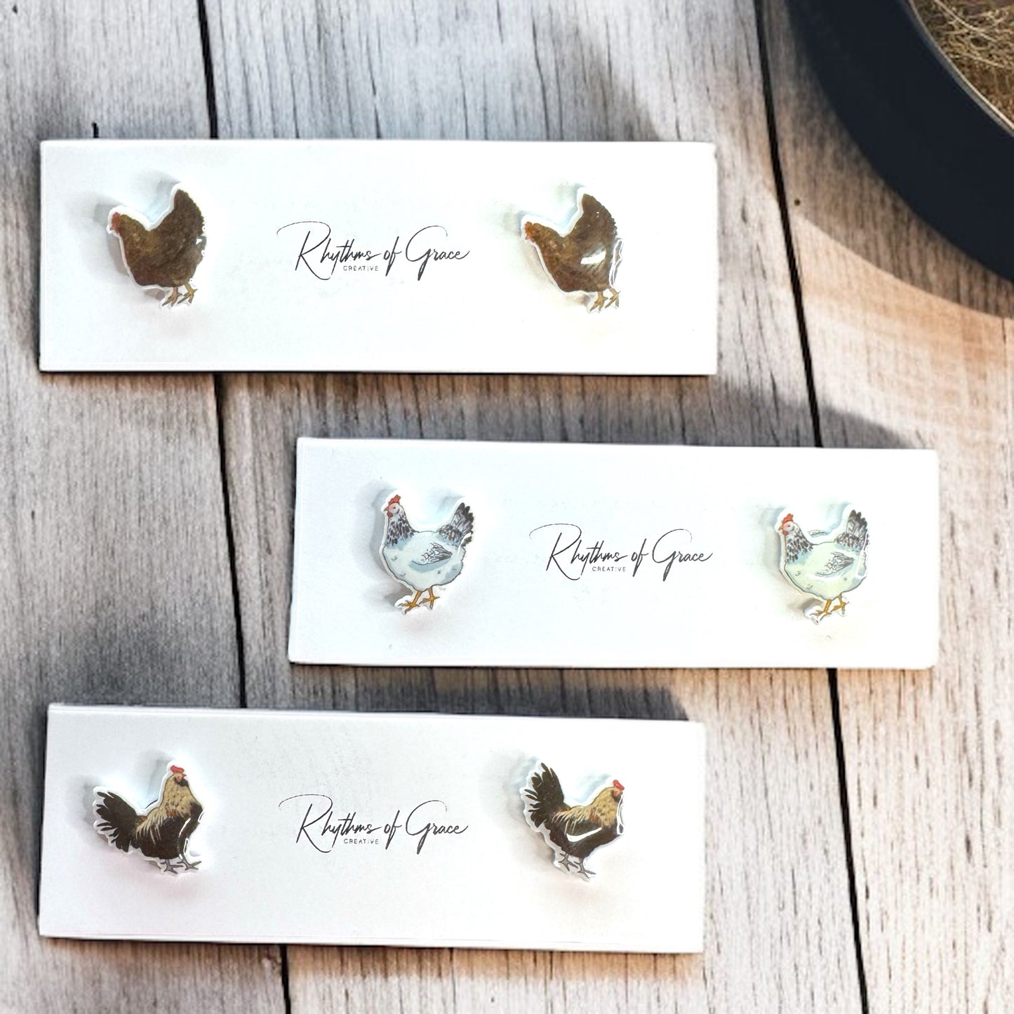 Set of chicken-themed earrings on branded cards on a wooden surface