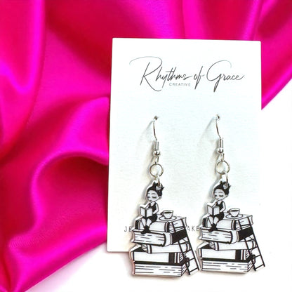 Black and white book-themed earrings on a pink satin background with 'Rhythms of Grace Creative' branding.