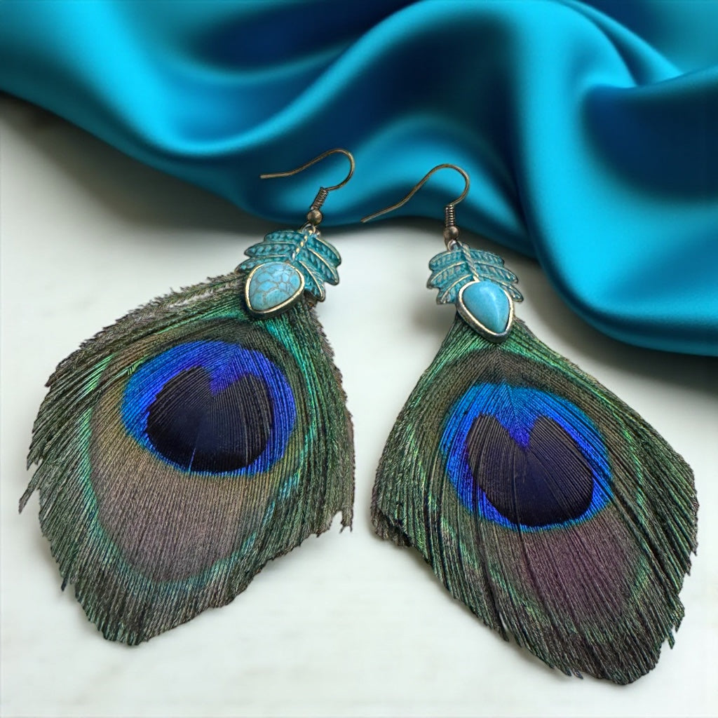 Peacock feather earrings with turquoise stones on a blue fabric background