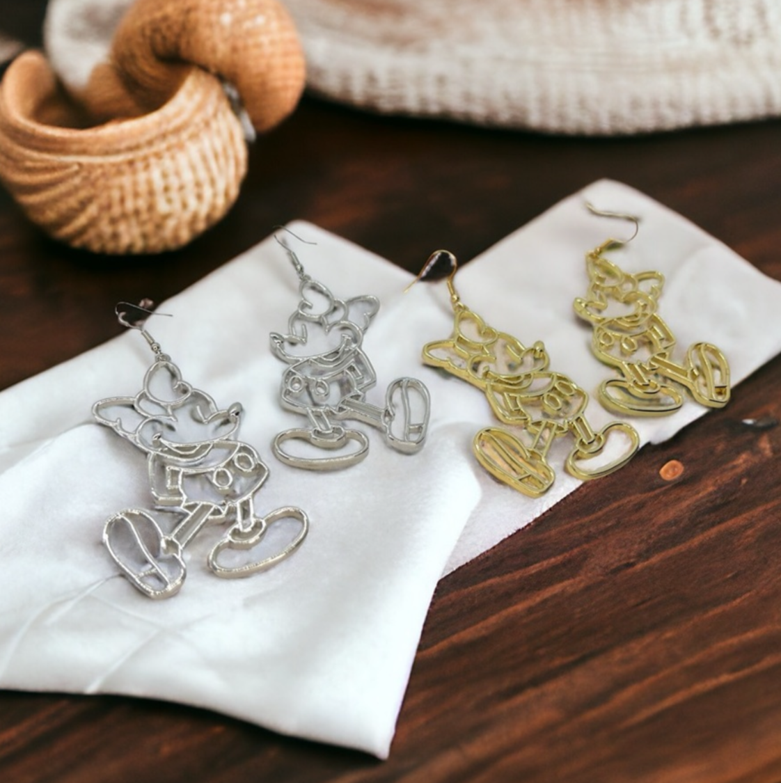 Pair of silver earrings on a white cloth with a wooden surface and woven basket in the background.