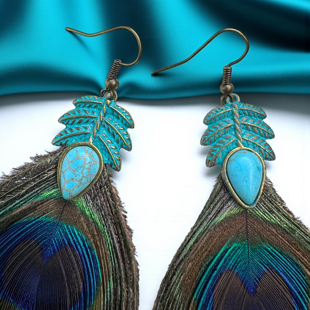 Pair of earrings with turquoise stones and feather details on a blue fabric background