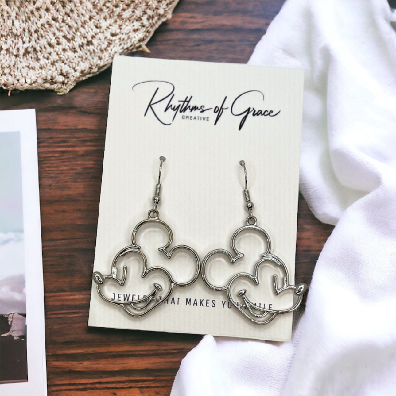 Pair of silver earrings on a 'Rhythms of Grace' branded card with a white cloth background.