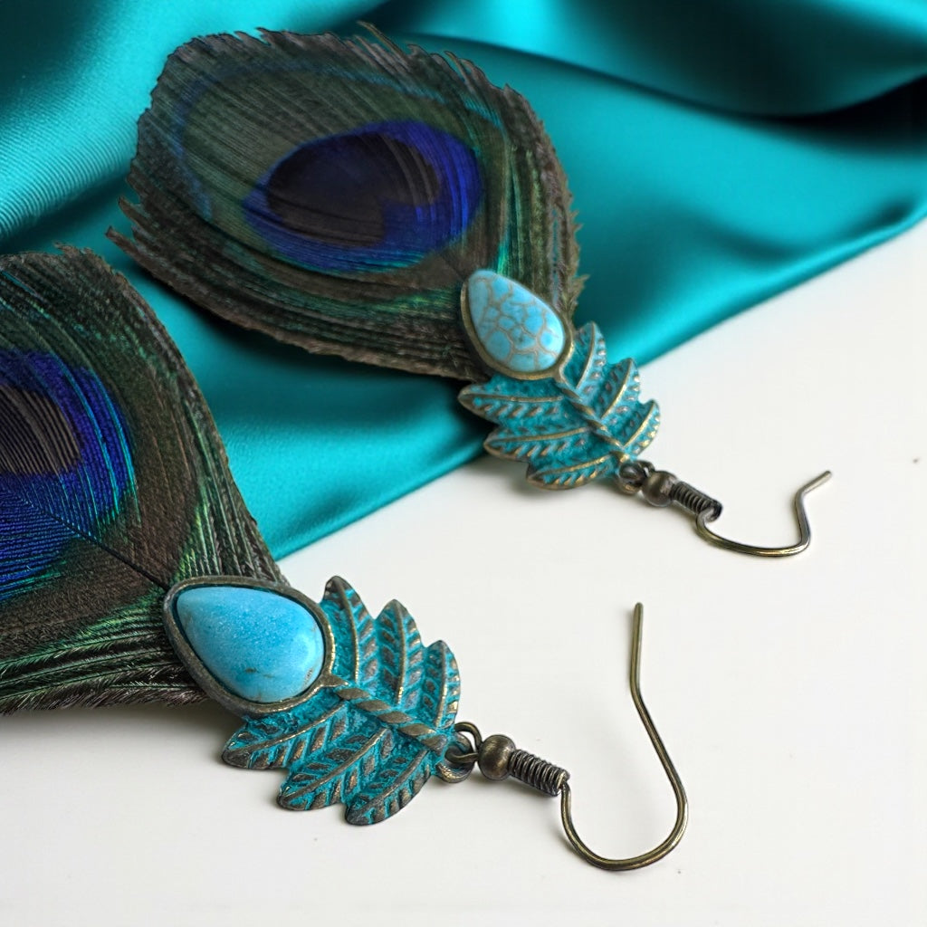 Pair of peacock feather earrings with blue stones on a turquoise fabric background