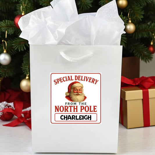 White gift bag with Santa Claus label in front of a Christmas tree
